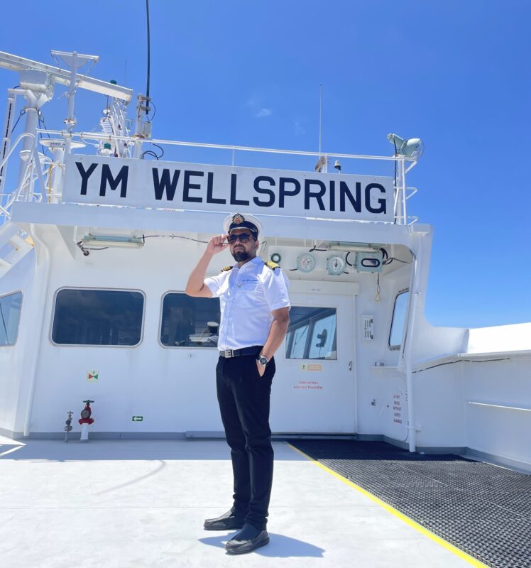 Captain stands on deck of a large container ship on a blue sky day.