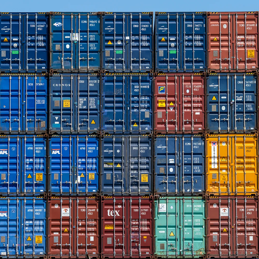 Stacked colorful shipping containers arranged in rows under a clear blue sky.