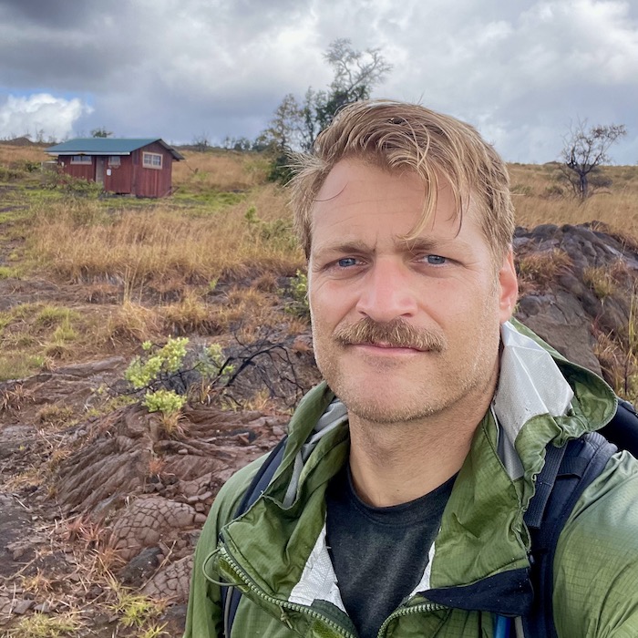 Man in raincoat outside in an open field on a cloudy day.