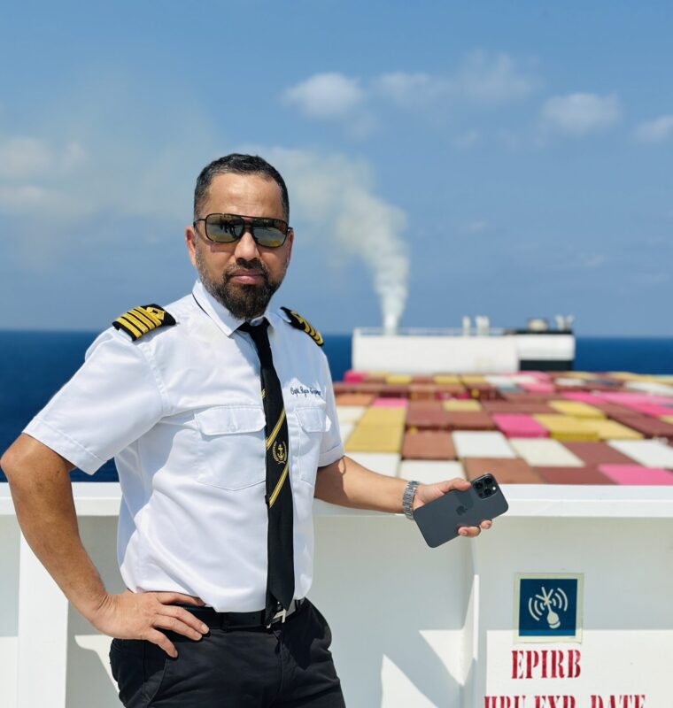 Captain Ryan standing on deck of a container ship with shipping containers in background.