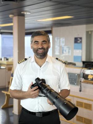 The Captain of a container ship stands with a large camera.