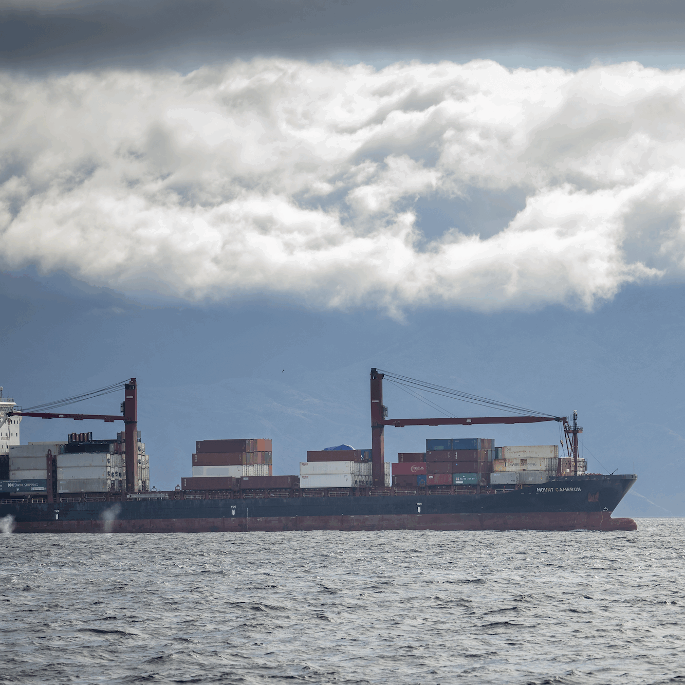 009_©CLEVENGER-231117 copy A large container ship on a partly cloudy day with two whale spouts closeby.