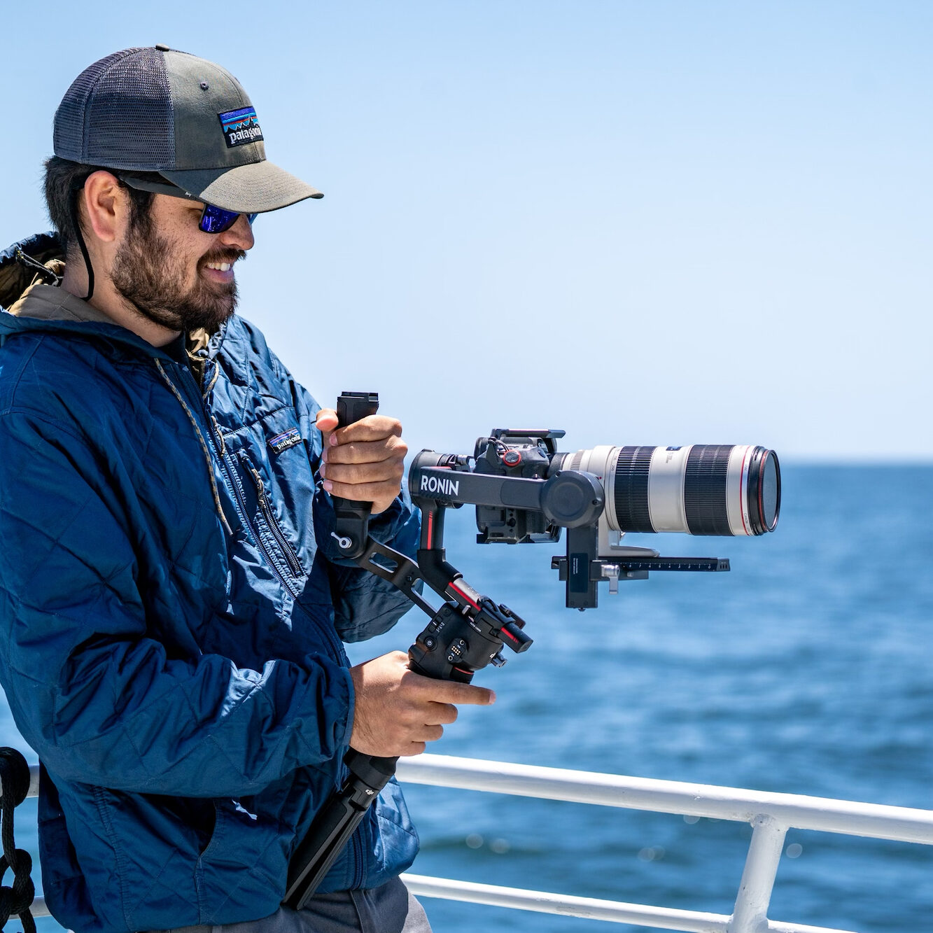 Man on a boat out on the ocean holding professional camera gear and appears to be photographing something in the ocean.