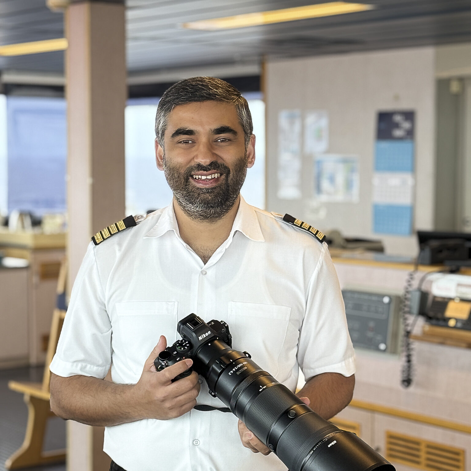 The Captain of a container ship stands with a large camera.