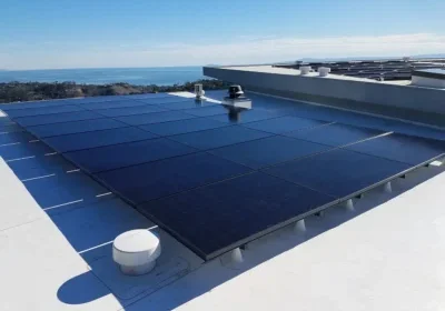 Solar panels installed on a flat rooftop with a clear sky and distant ocean view.