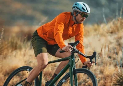 Man in orange jacket and helmet riding a bicycle outdoors on a grassy trail.