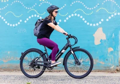 Woman wearing a helmet rides a bicycle past a blue mural with white and yellow dots, carrying a backpack.