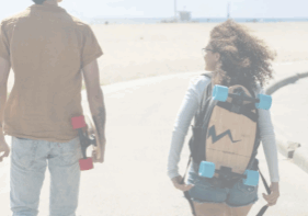 Two people walk on the boardwalk on the sand with skateboards in hand.