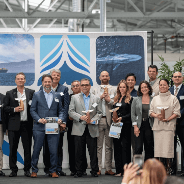 A group of people pose on stage holding awards at an indoor event with a blue and white backdrop.