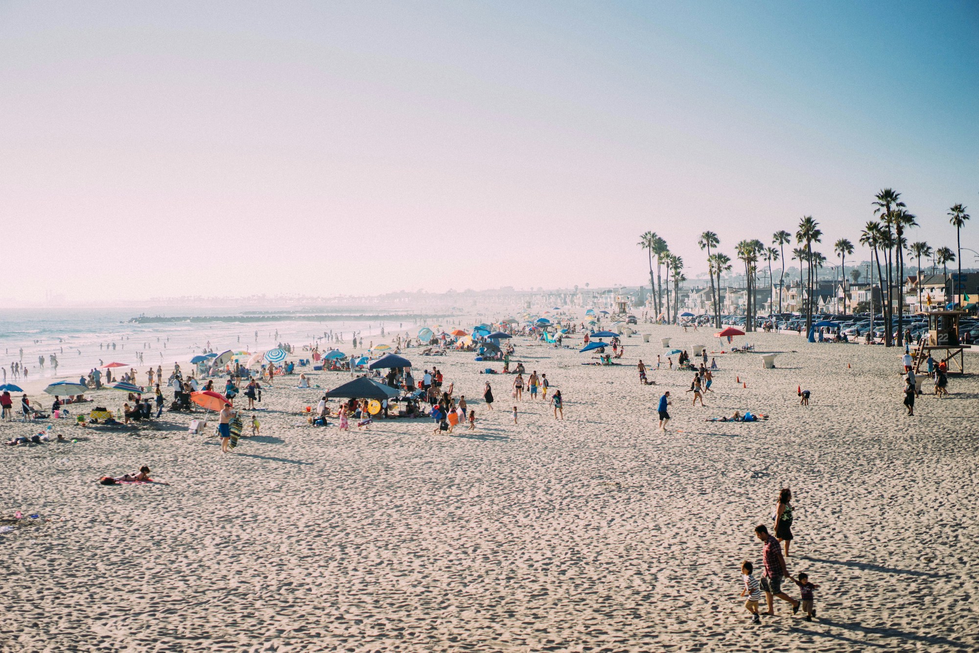 Wide shot of the beach on a busy day with many groups of people and a family walking in the foreground in a Southern California location.